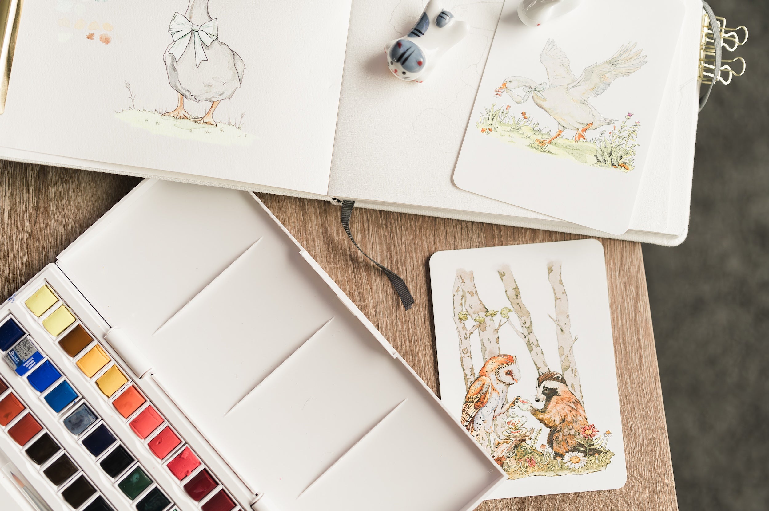 Julia Hope’s art desk with watercolor supplies, whimsical animal illustrations, printed art cards, and nature-inspired artwork in progress.